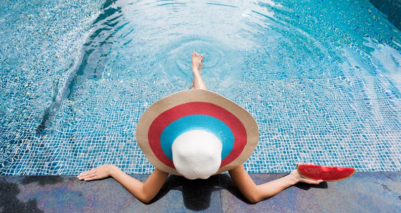 Eine Frau mit Hut entspannt sich am Pool mit Melone
